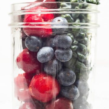 Acai, cherries, blueberries, and kale meal prepped for the freezer in a glass mason jar