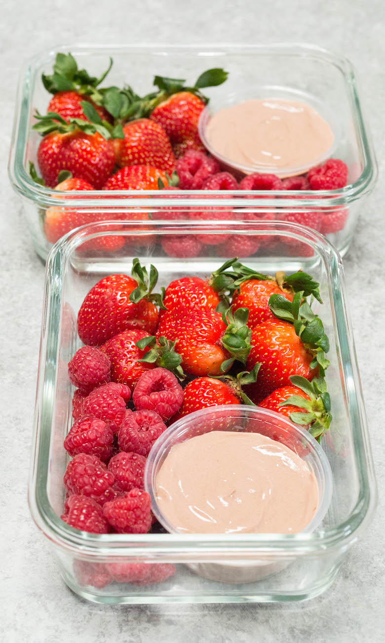 Two glass meal prep containers on a white background filled with chocolate greek yogurt fruit dip and strawberries and raspberries