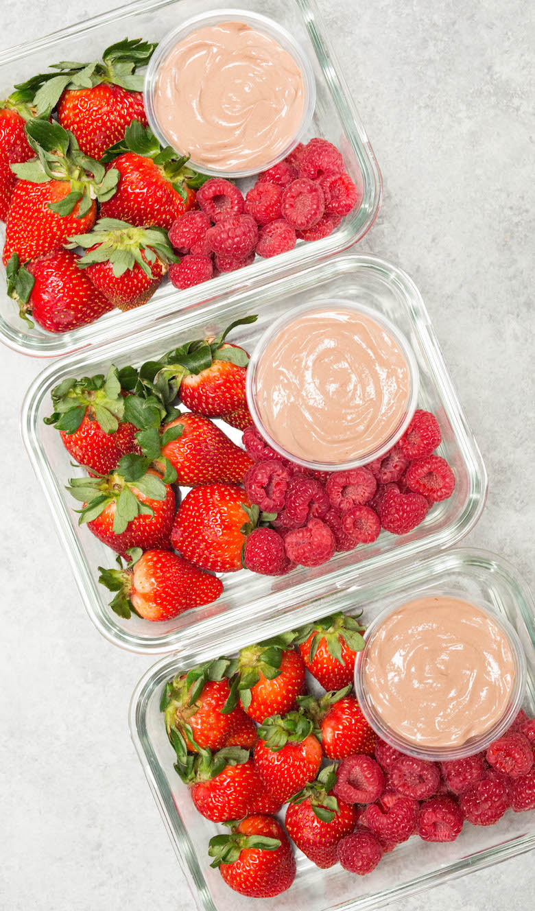 Three glass meal prep boxes with a round container of chocolate greek yogurt fruit dip surrounded by strawberries and raspberries