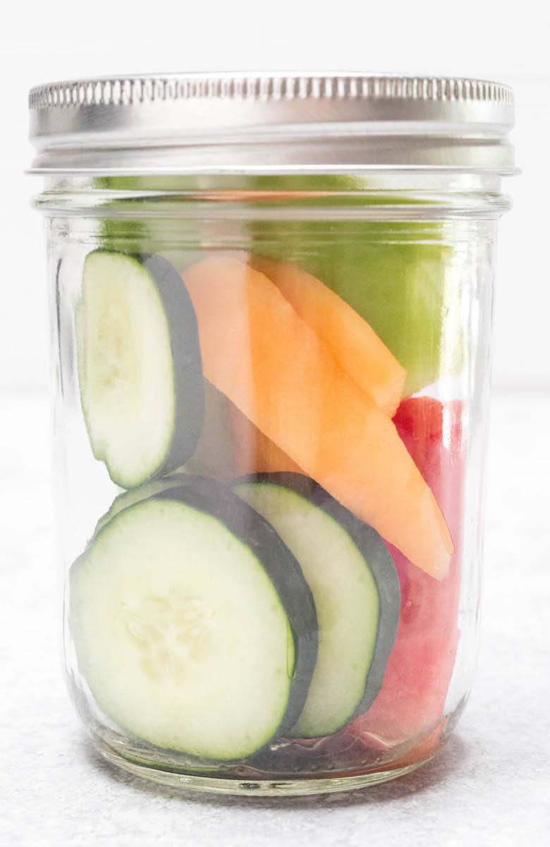 Close up of a glass jar with hydrating melon smoothie ingredients on a white background