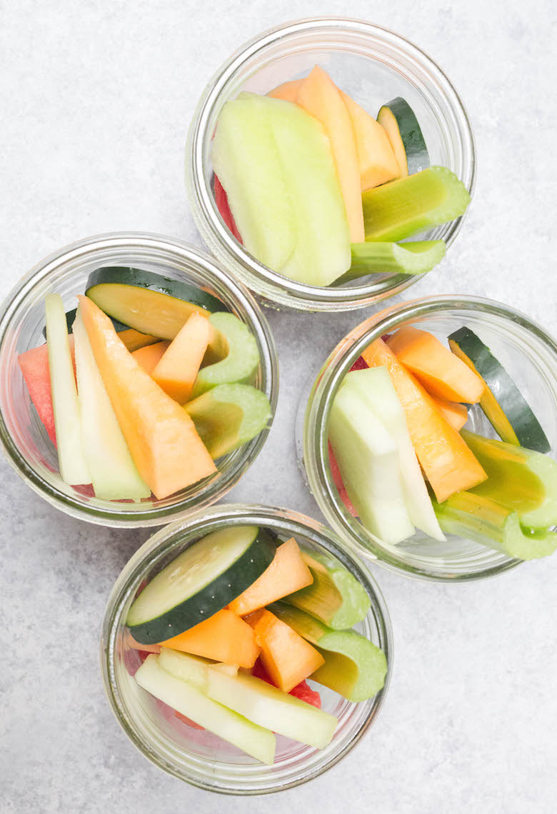 Overhead view of 4 mason jars filled with melon smoothie freezer pack ingredients