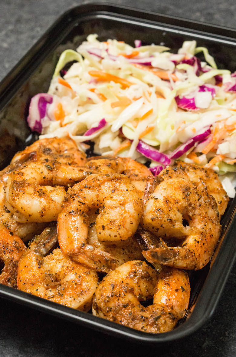 A black meal prep container filled with blackened shrimp and coleslaw