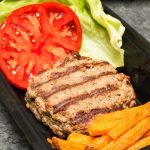 Meal prep container with sweet potato fries, a hamburger patty, lettuce, and tomato