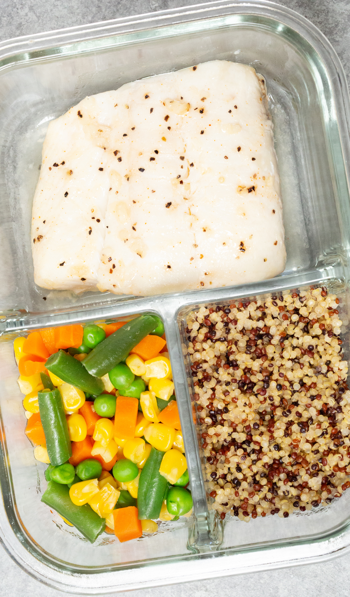 A single glass meal prep container filled with a fish fillet, mixed vegetables, and quinoa.