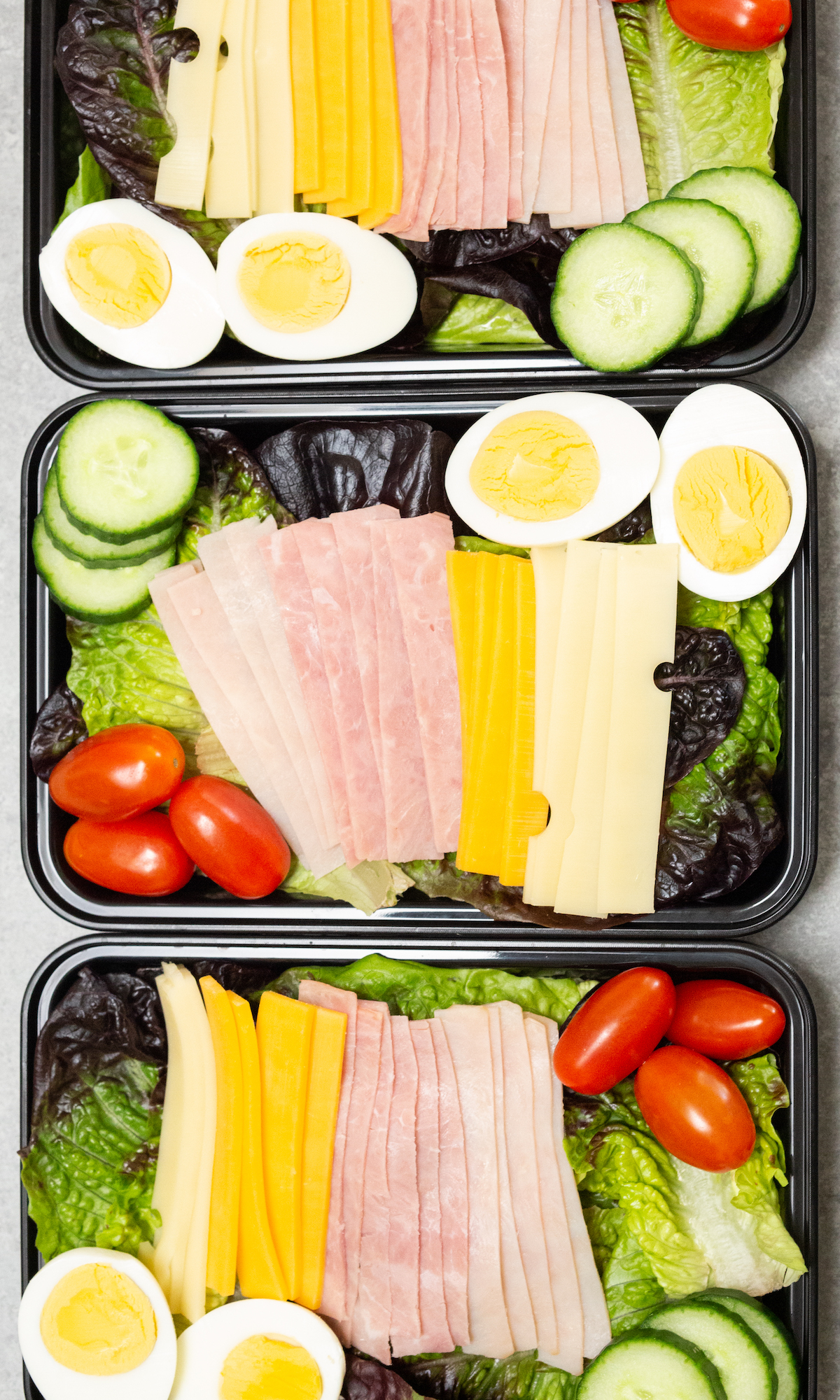 Overhead look at three black plastic meal prep containers filled with chef salads.