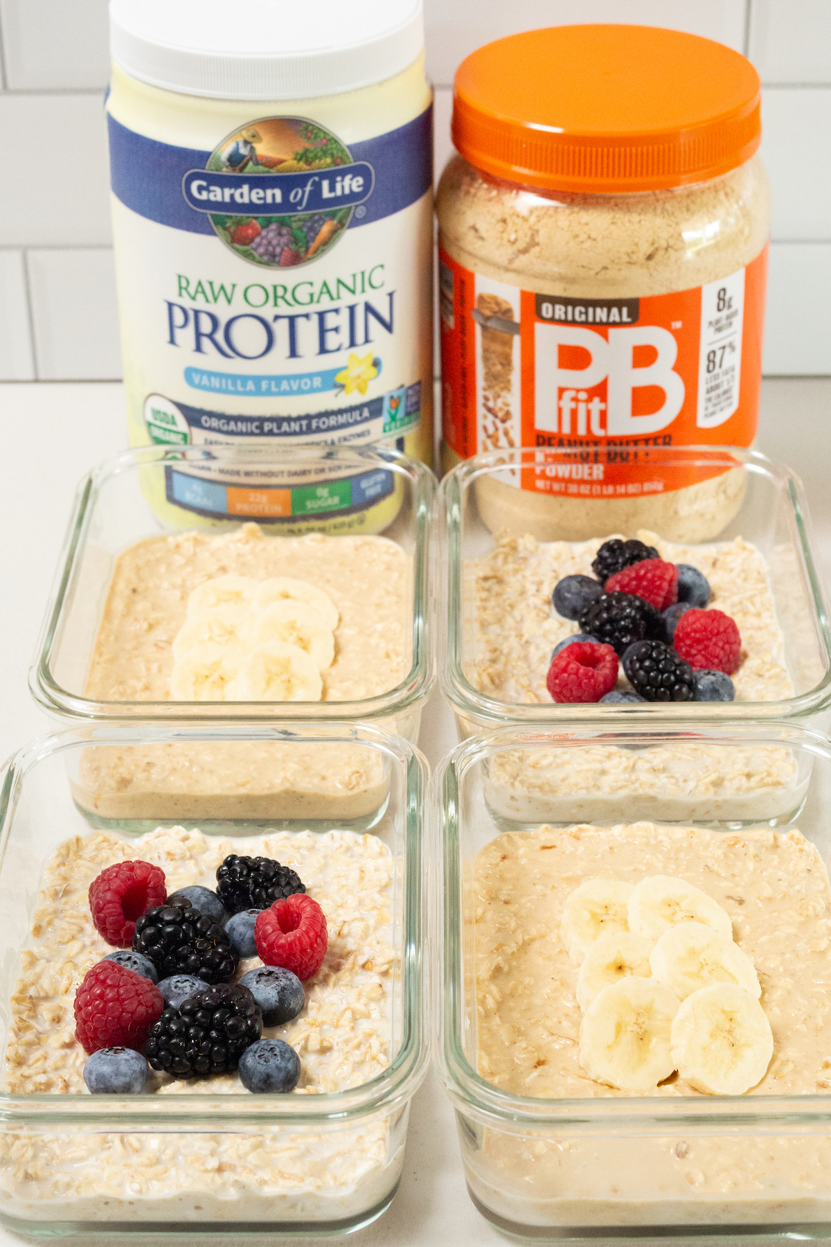 Four glass meal prep containers with overnight protein oats in front of vanilla protein powder and PB2 peanut butter powder.