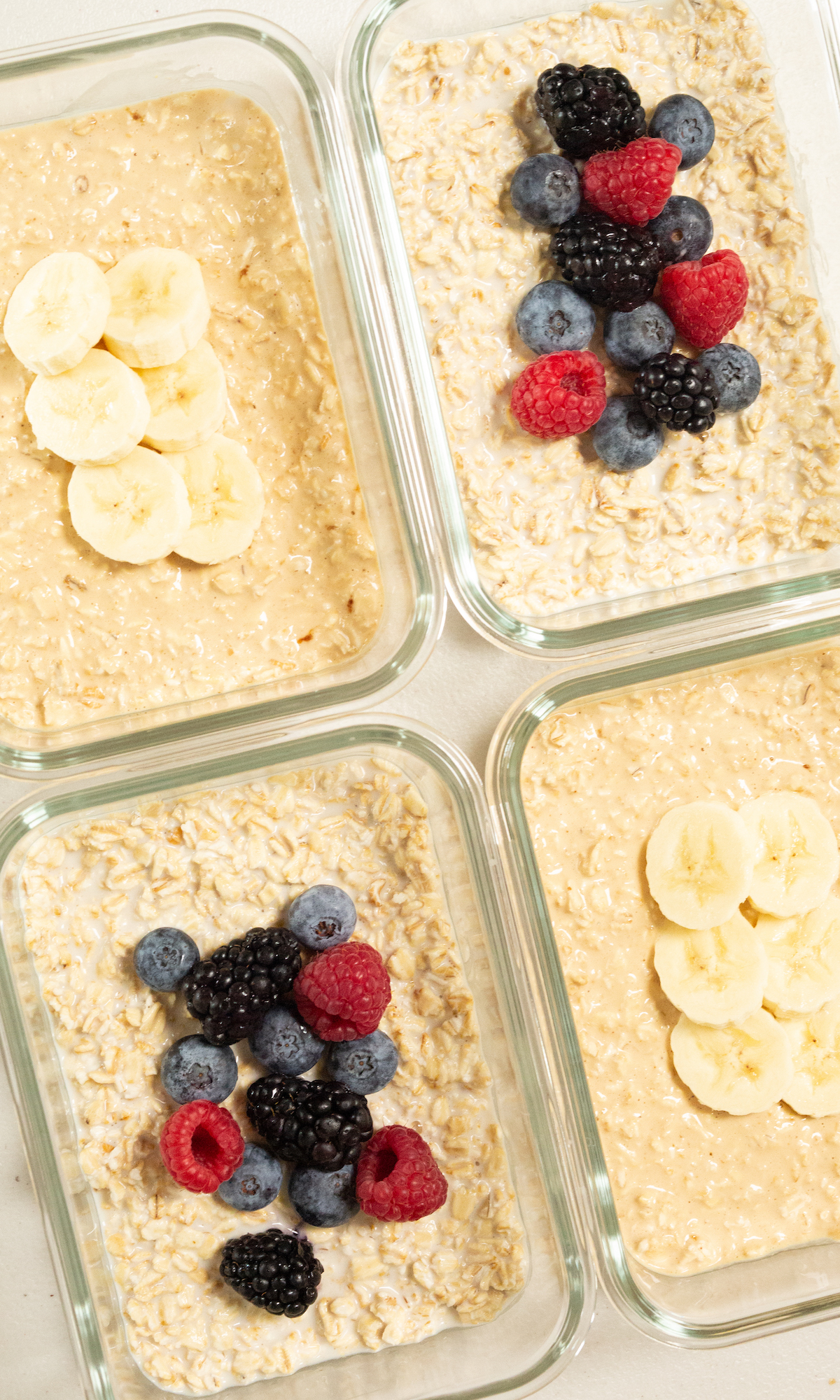 Overhead view of four glass sqaure meal prep containers filled with protein overnight oats topped with berries and bananas.