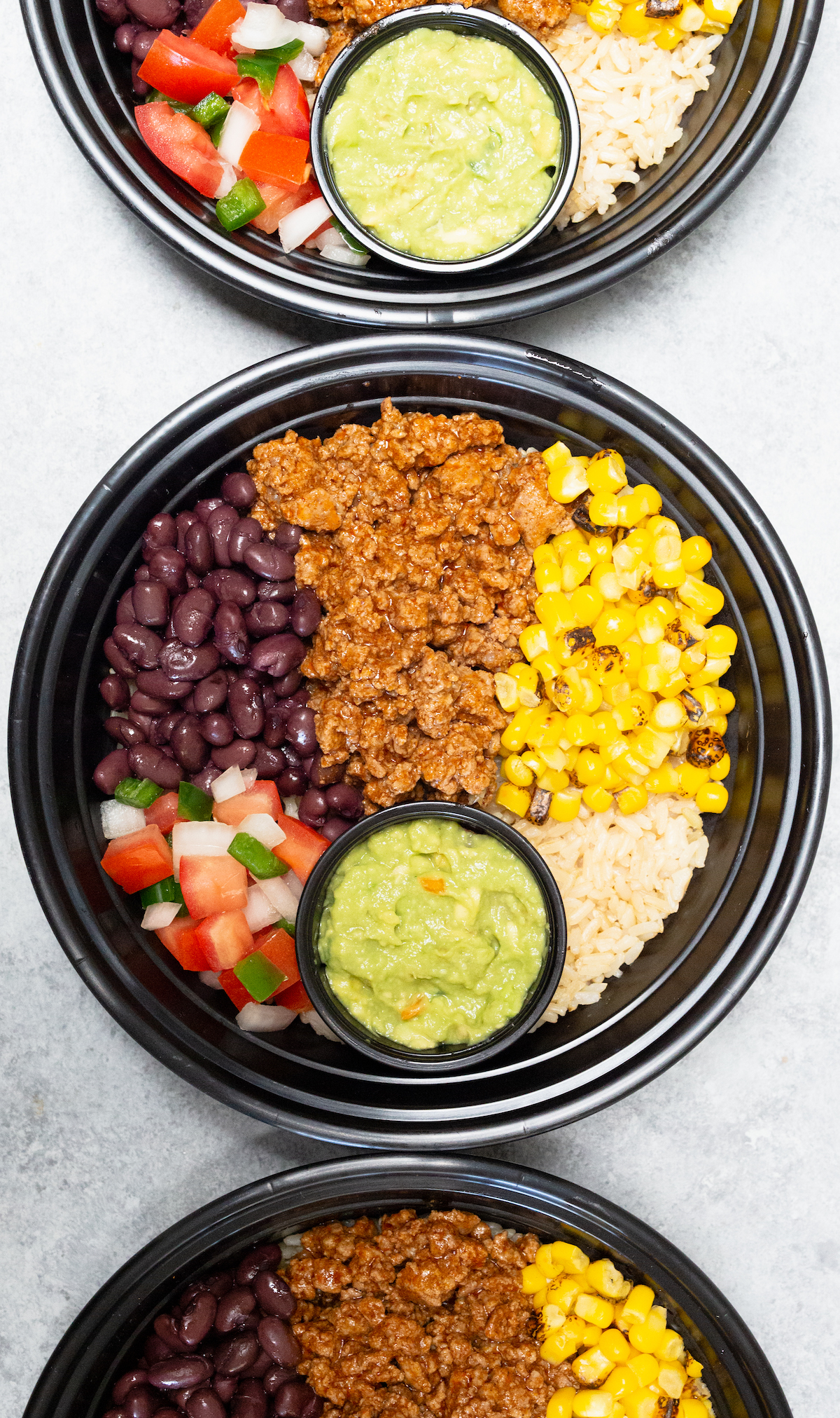 Overhead three plastic meal prep bowls filled with ground beef, corn, and bean taco bowls.