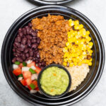 Overhead three plastic meal prep bowls filled with ground beef, corn, and bean taco bowls.