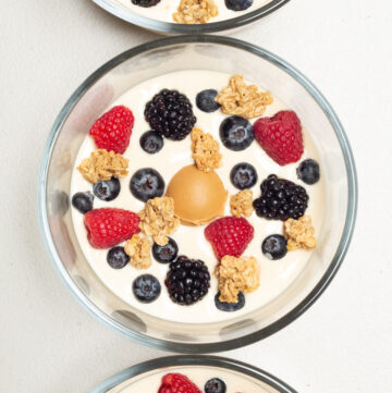 Overhead view of three small glass bowls each fulled with light brown peanut butter yogurt, then topped with fresh berries and granola.