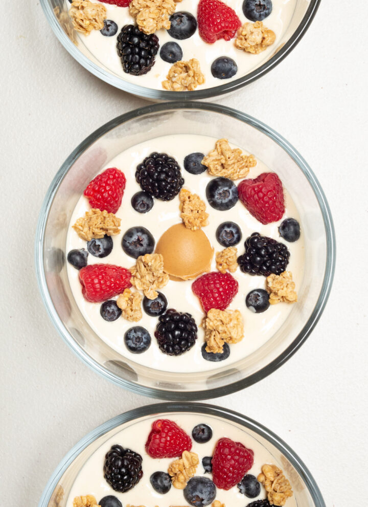 Overhead view of three small glass bowls each fulled with light brown peanut butter yogurt, then topped with fresh berries and granola.