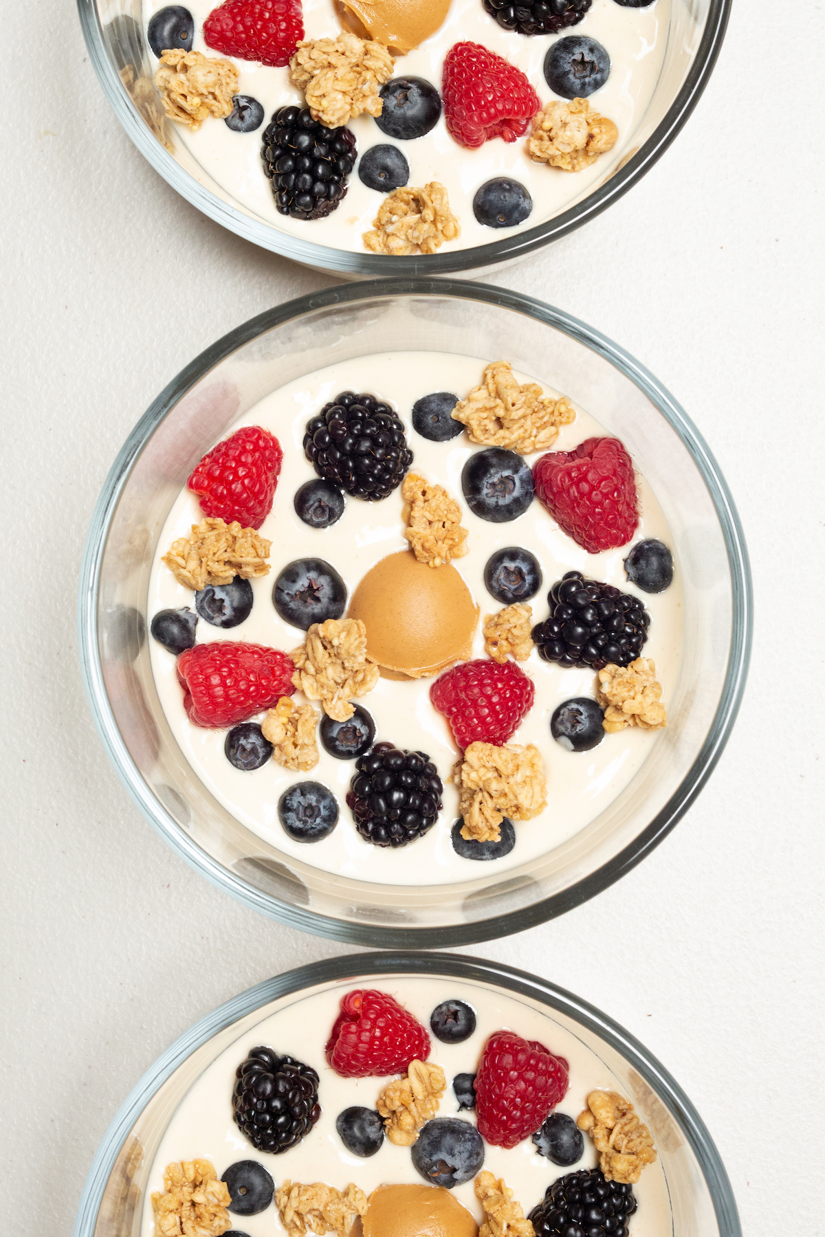 Overhead view of three small glass bowls each fulled with light brown peanut butter yogurt, then topped with fresh berries and granola.